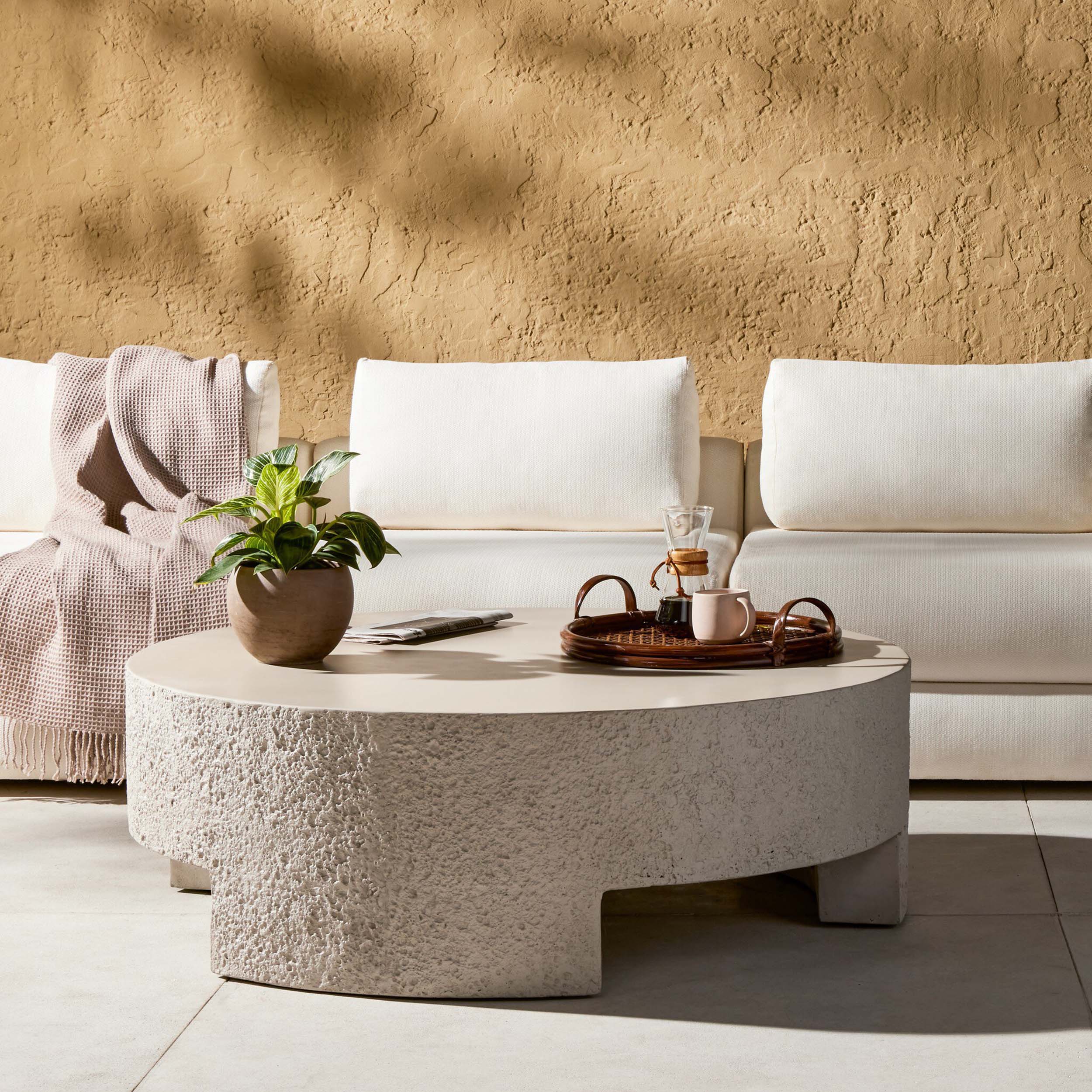 Kember Outdoor Coffee Table, Matte Stone in an outdoor setting with modern decor elements.