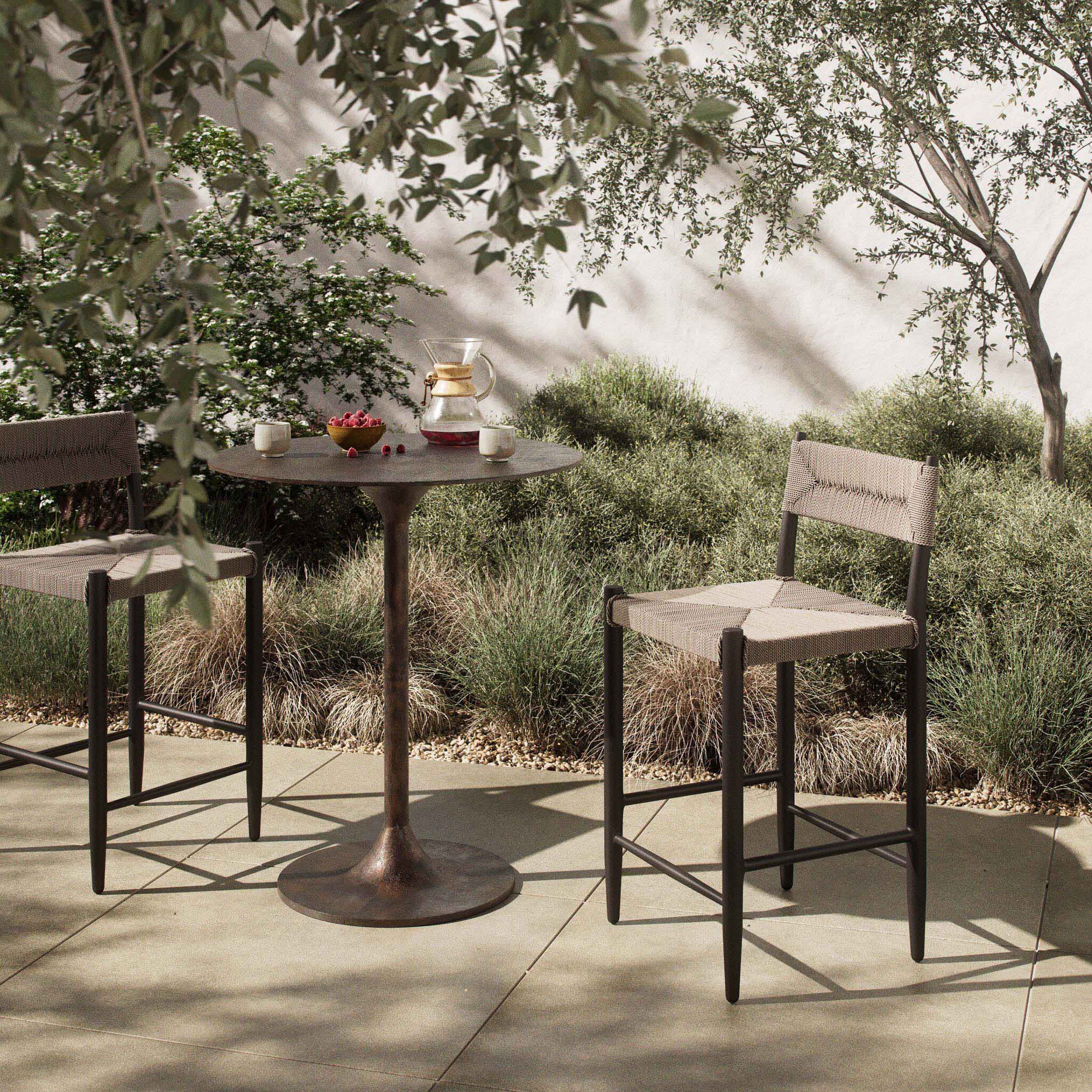 Lomas Outdoor Metal Bar + Counter Stool, Textured Dune showcased in a serene outdoor seating arrangement.