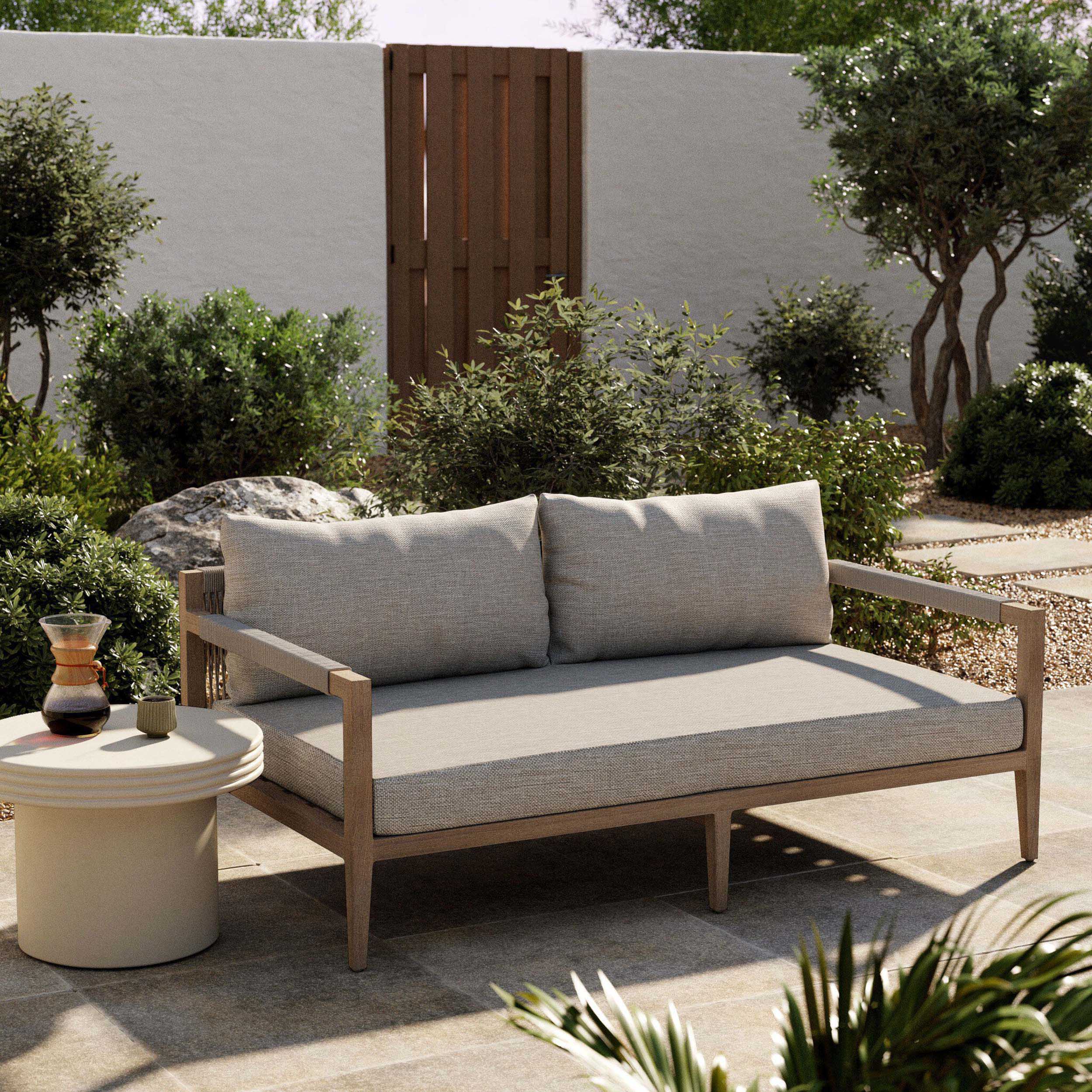 Sherwood Outdoor Sofa, Washed Brown, Venao Charcoal in a modern outdoor setting with lush greenery.
