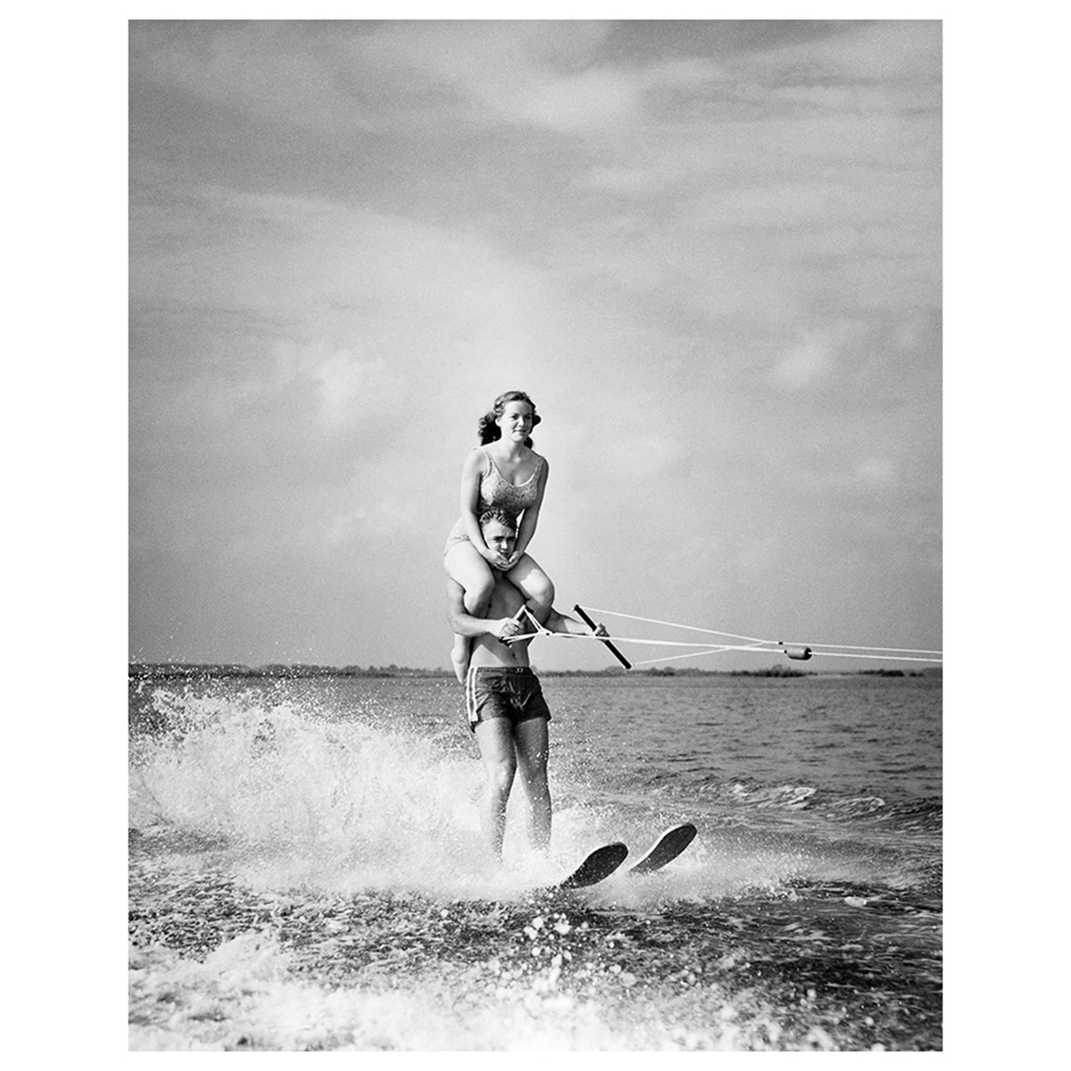 Young man Waterskiing in sea with young woman sitting on his shoulders